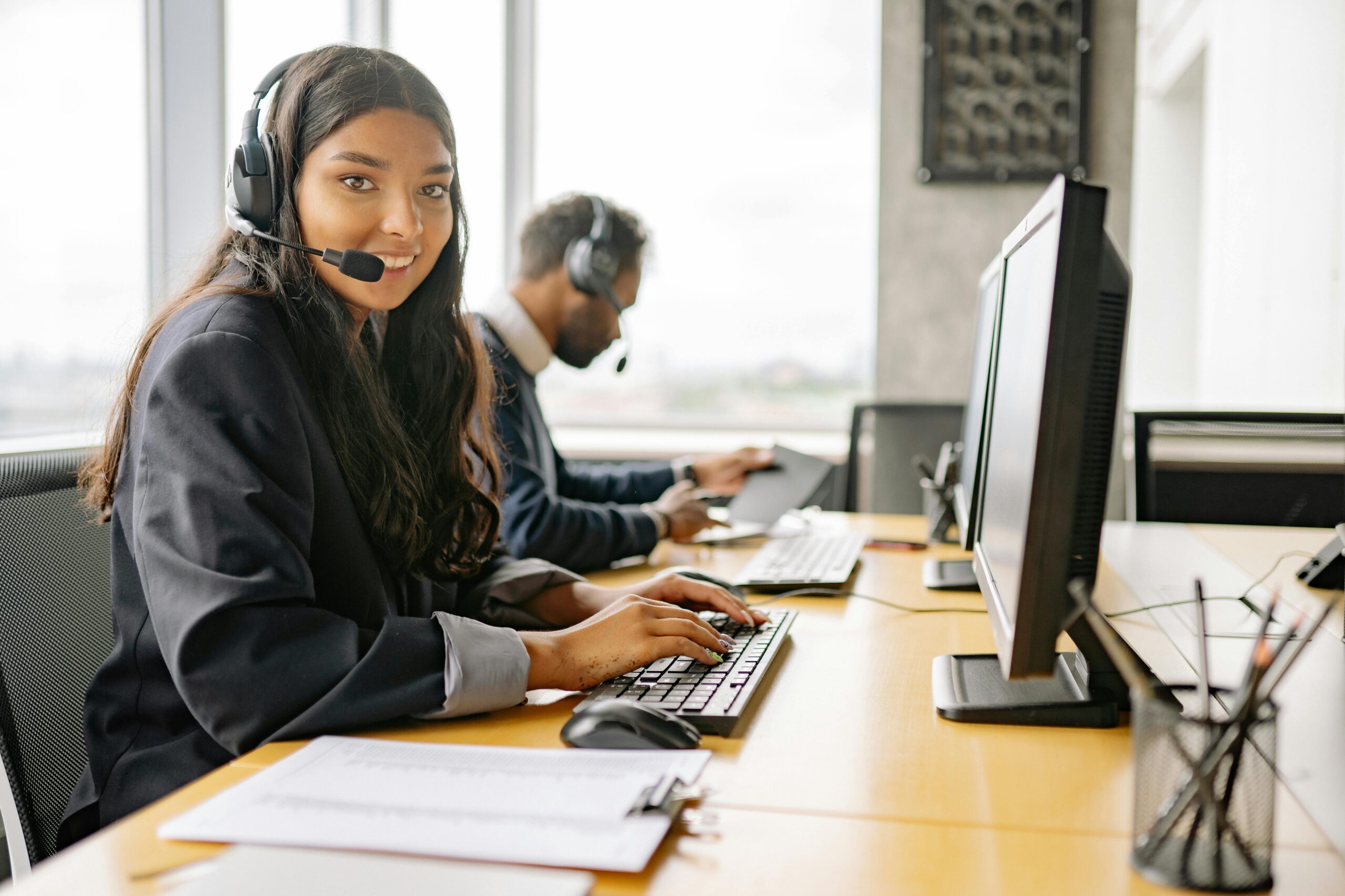 Friendly customer support agent with headset smiling at her desk, offering personalized travel assistance.